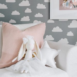 a alimrose gold angel bunny doll with white skirt and bow with gold wingssitting on couch with cloud wallpaper background
